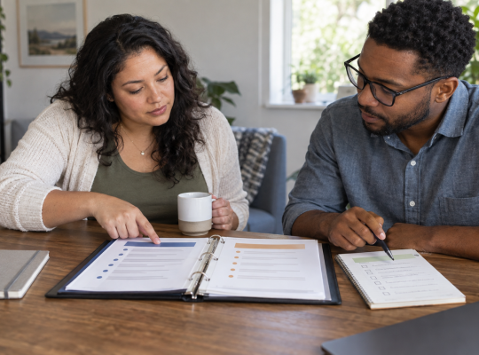 Two teammates compare an official binder with an informal checklist at a table.